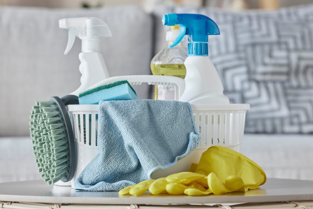 cleaning products, brush and basket on table in home living room for housekeeping. hygiene, spring cleaning and cleaning supplies, gloves and chemicals for disinfection, germs or bacteria prevention.